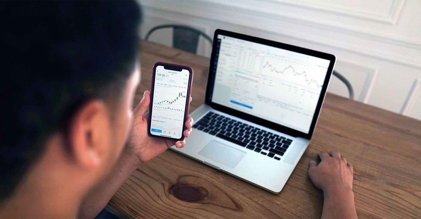 young man looking at stocks on phone and computer